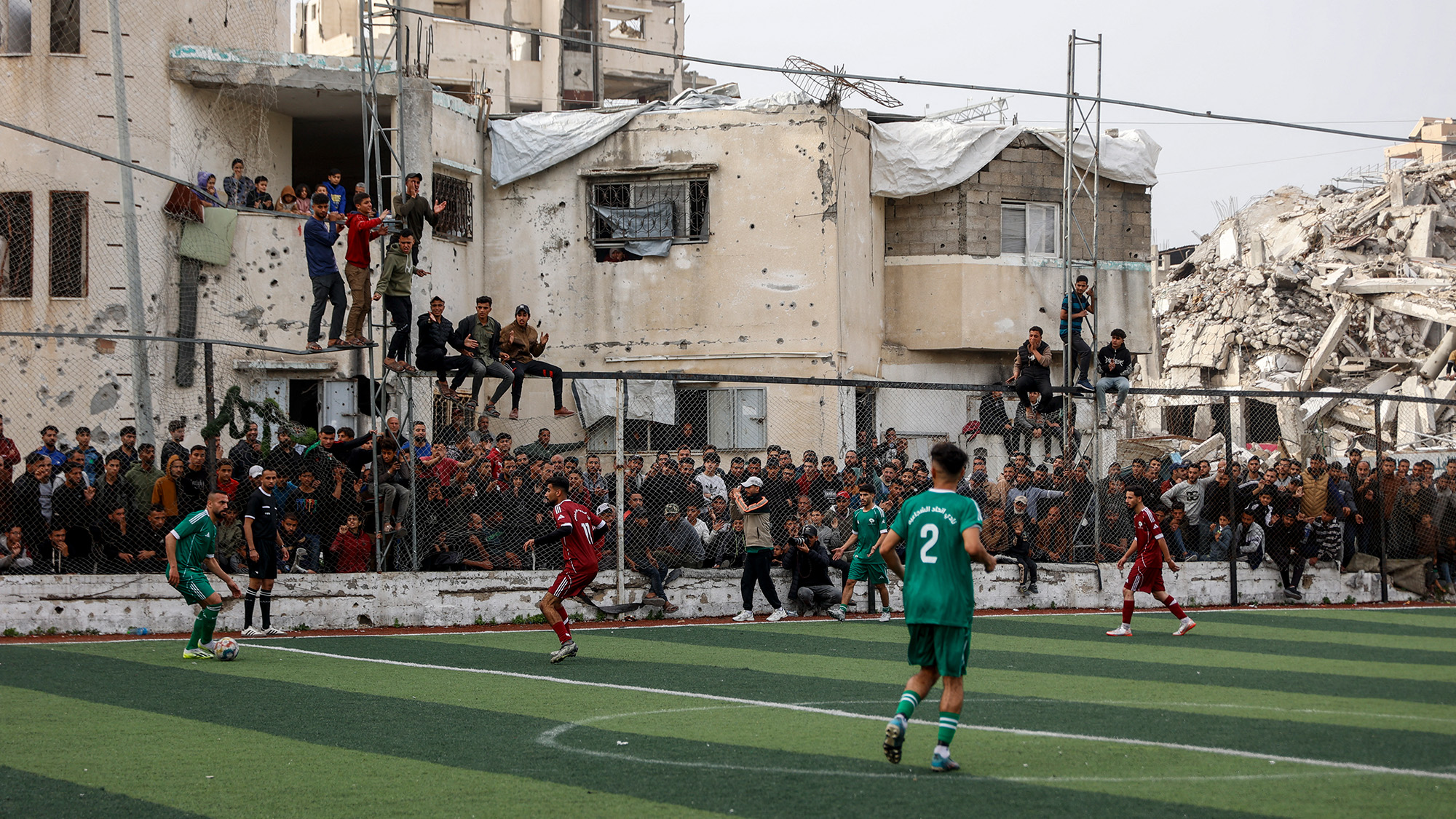 Palestinians watch a football match amid the rubble of destroyed buildings in Gaza City, Palestine