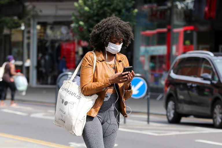 Woman on phone, walking along the street and wearing a face mask