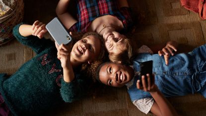 teenage skin issues - three teens lying on the ground looking at their phones smiling - gettyimages995393002