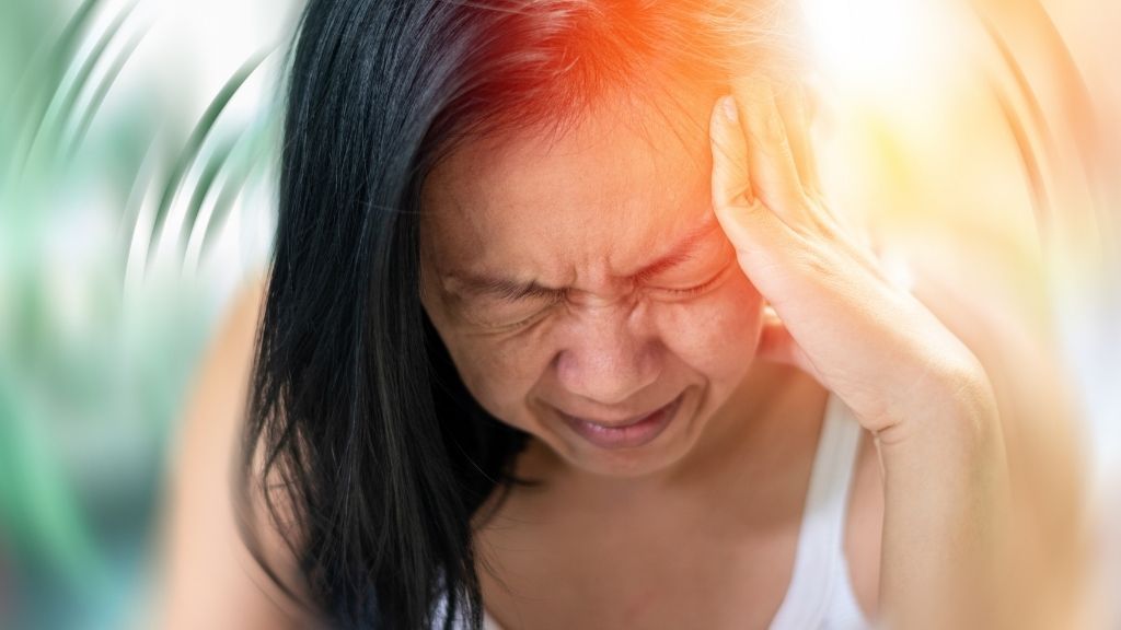 Woman holds her head in both hands with her eyes closed; the background is blurred around her as if she&#039;s spinning or dizzy