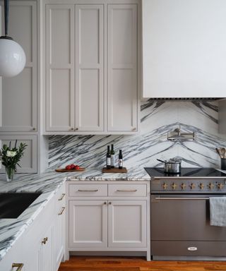 Prominently veined marble countertops and backsplash in a neutral kitchen