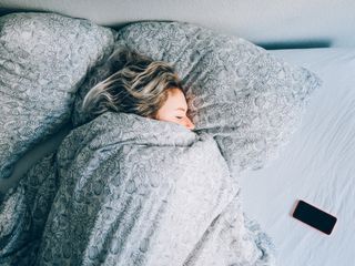 Woman in bed with smartphone beside her using white noise for sleep