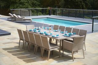 A dining area beside a swimming pool with a glass surround and loungers