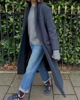 woman wearing cuffed denim outfit with navy long coat and adidas sneakers