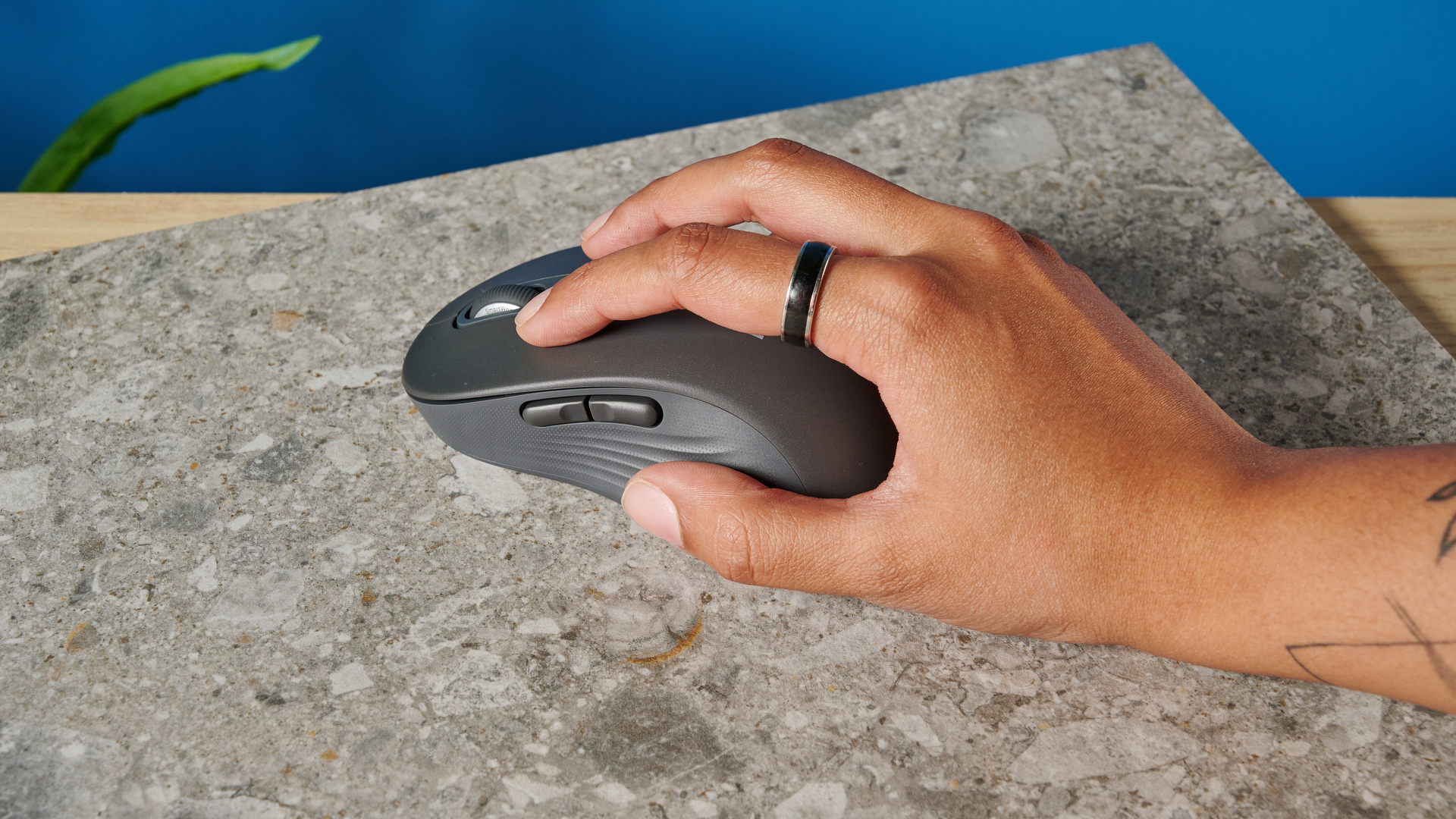 a black mouse with a scroll wheel, two side buttons, and grooved edges, with a logi logo, sits atop a pale table with a blue background