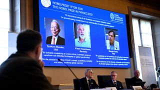 Representatives from the Royal Swedish Academy of Sciences sit in front of a screen displaying the winners of the 2021 Nobel Prize in Physics.