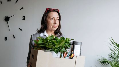 Mature businesswoman holding box with office belongings after being laid off 