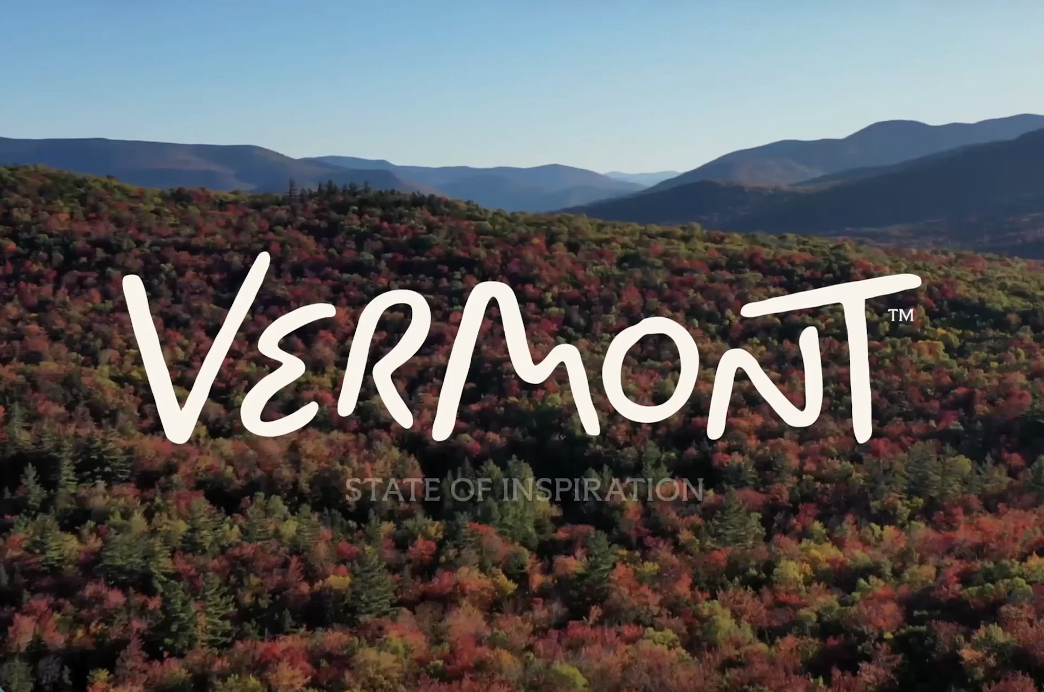 Aerial view of autumn-coloured Vermont hills and distant mountains, overlaid with the hand-lettered "Vermont" wordmark and the strapline "State of Inspiration".