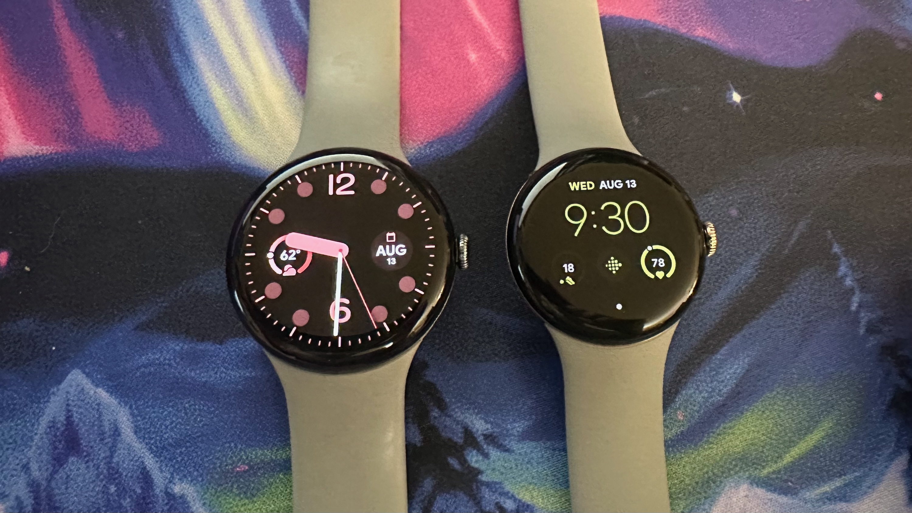 The Google Pixel Watch 3 45mm (left) and 41mm (right) sitting on a desk mat side-by-side, both showing a standard watch face.