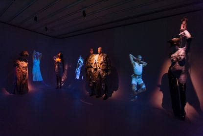 View of the Claire Barrow and Galeria Melissa installation featuring dressed and artistic mannequins and images projected onto the wall in a dark room