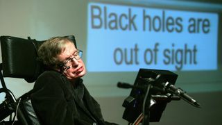 a man sits in a wheelchair in front of a presentation slide that reads "black holes are out of sight"