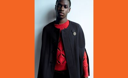 Model wears Stefan Cooke A/W 2021 menswear black cape and deconstructed red jumper