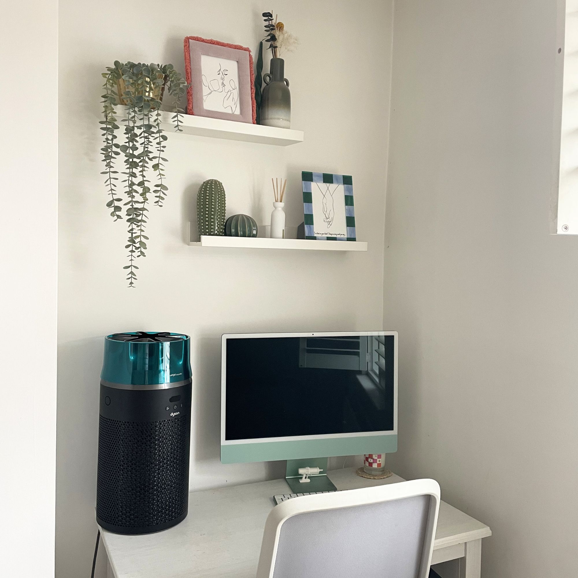 Dyson Hushjet Air Purifier sitting on a white desk next to a green computer and shelves above it