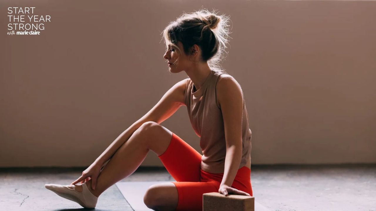 A woman on her phone in gym wear prior to doing some of the best Pilates exercises