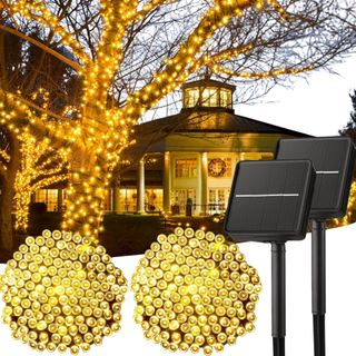 Warm light solar powered Christmas lights wrapped round a tree in front of a house