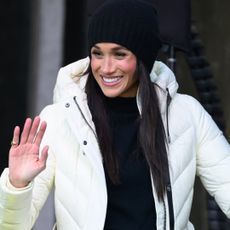 Meghan Markle wearing a white puffer coat and smiilng and waving