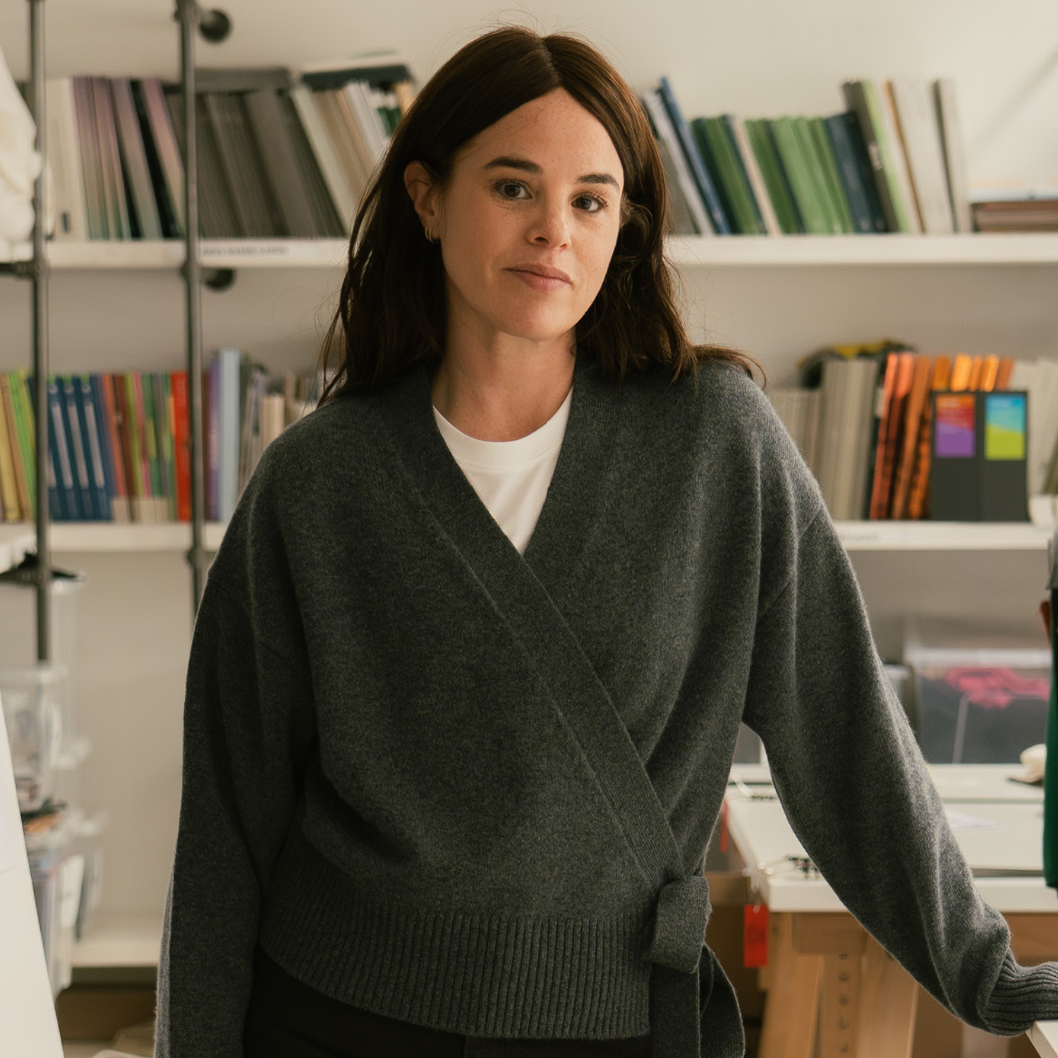 A woman with short brown hair in a white t-shirt and a wrap gray sweater