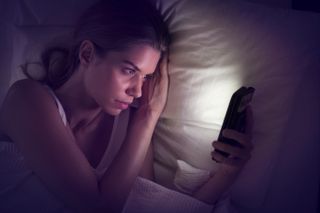 Young woman looking at smartphone in bed - stock photo