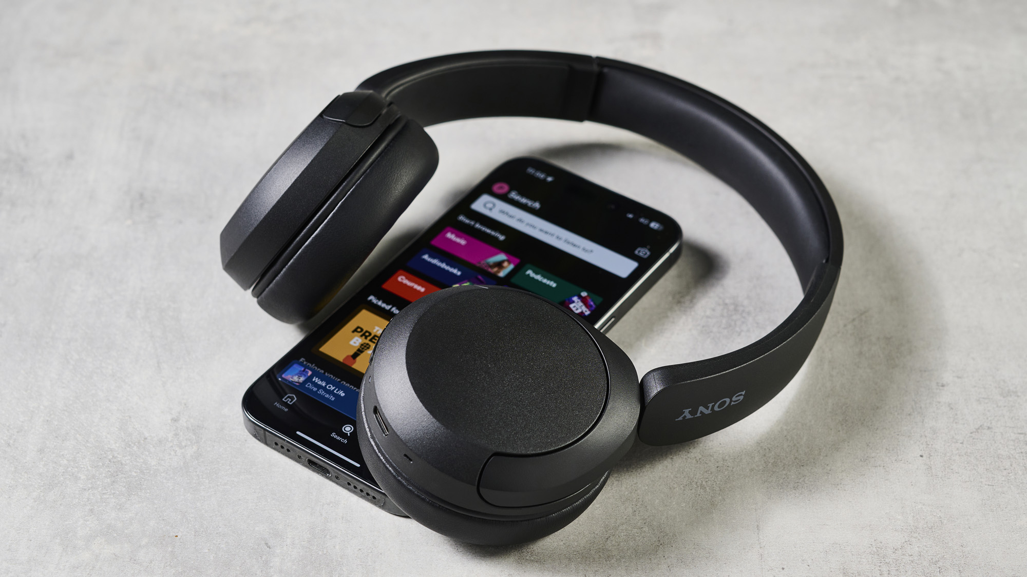 A photo of the Sony WH-CH520 over ear headphones next to a phone with the Spotify app open
