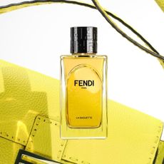 a yellow Fendi baguette perfume in front of a yellow fendi baguette bag on a plain backdrop