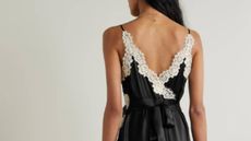 A female model facing away, wearing a black satin dress with white lace detailing and a black bow at the back, from NET-A-PORTER.