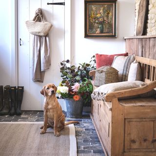 hallway with flagstone slate floor natural material rug with dog sat on rug and antique monks bench seating coat hung on the back of white door
