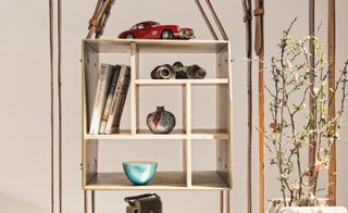 Flowers, model car, binoculars and books on wooden shelf suspended between leather belts on display unit