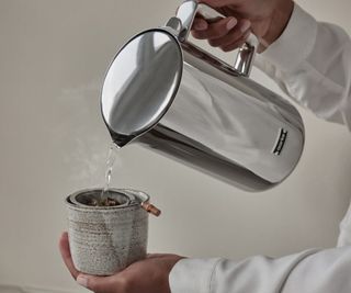 Water pouring from the Aarke Kettle into a cup held against a beige background.