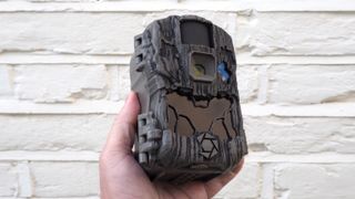 Stealth Cam DS4K Ultimate Trail Camera held in a hand in front of a white brick wall