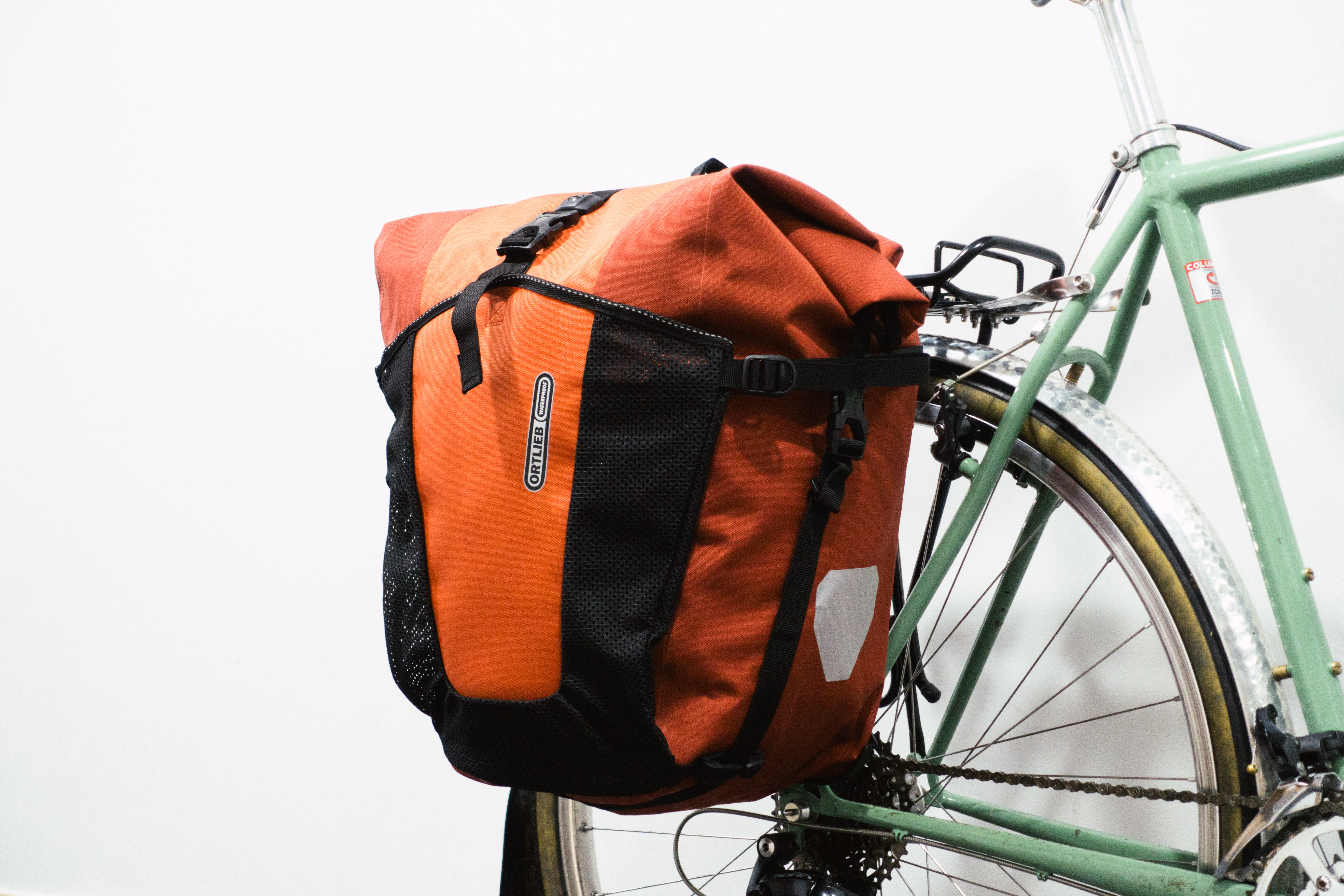 A very large orange pannier mounted to a green bike against a white background