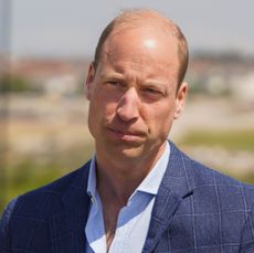 Prince William looking serious wearing a blue suit jacket outside 