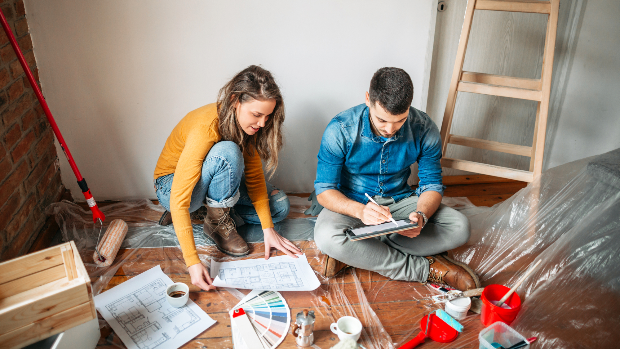 male and female sat on floor looking at colour charts, papers and a tablet with DIY tools and equipment around them