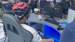 An attendee at WAIC 2026 in Shanghai sits in a chair wearing a brain-computer interface. The EEG has been mounted inside a bike helmet. They are using the BCI to play Black Myth: Wukong.