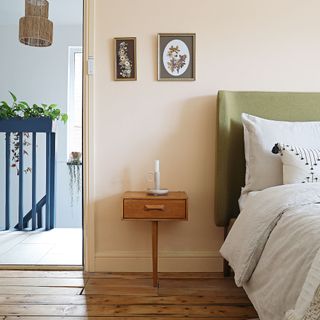 Bed with green headboard against a wall and skirting painted a pale salmon colour