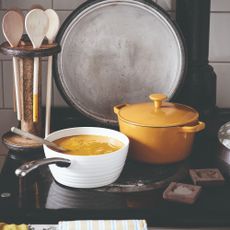 A kitchen with a soup cooking on the stove and a yellow casserole dish next to it
