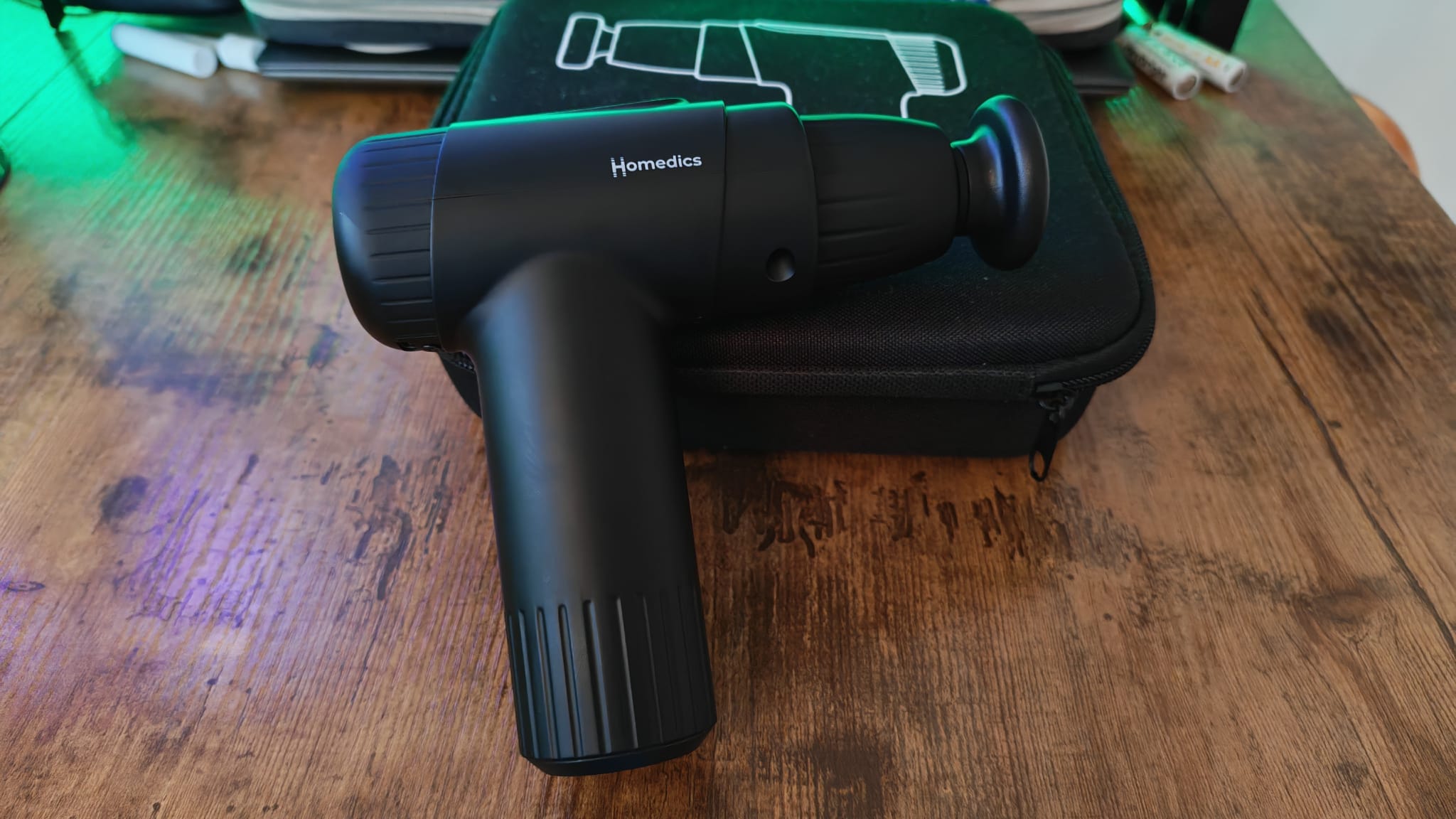 A Homedics massage gun on a wooden desk