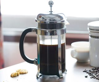 A French press on a table with coffee beans