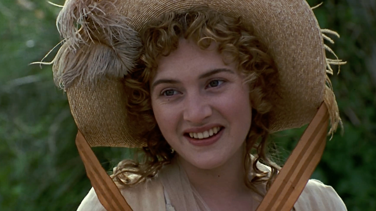 Kate Winslet smiles in the outdoors while wearing a fancy hat in Sense and Sensibility.
