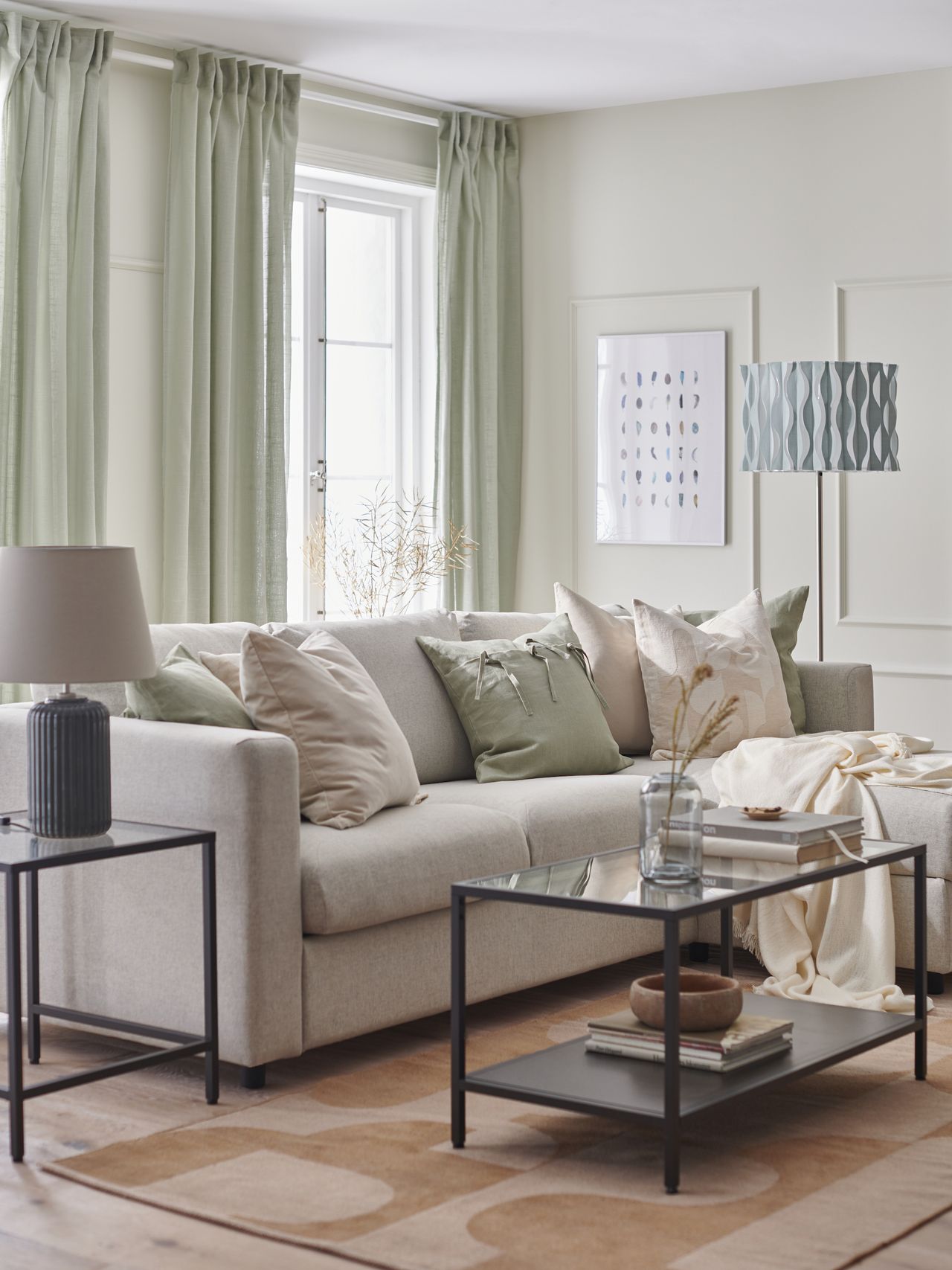 beige and pale green living room with black side and coffee table, patterned rug, pale green drapes, wooden floor, green and beige cushions and blanket