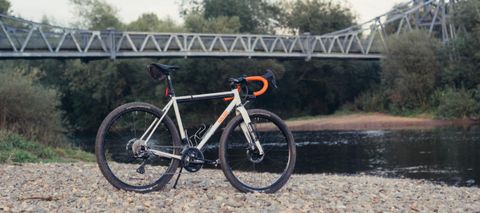 A white Fairlight Secan gravel bike on some rocks next to a river and a bridge