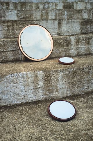 View of three round, wooden mirrors by Tiipoi pictured outside on steps during the day at the Varana Collective exhibition