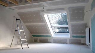 Large loft space with newly fitted insulating plasterboard around a large window with step ladder in foreground