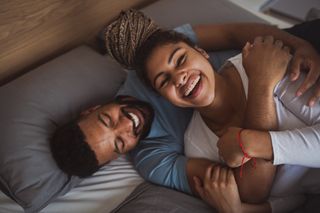 What is a soulmate? Portrait of young couple playing on bed indoors at home, laughing.
