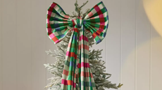 Anthropologie giant plaid bow tree topper crowning the top of a faux frosted Christmas tree, grounded by a wool-and-cotton-blend patchwork plaid skirt.