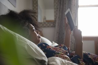 Woman lying down in bed with tablet