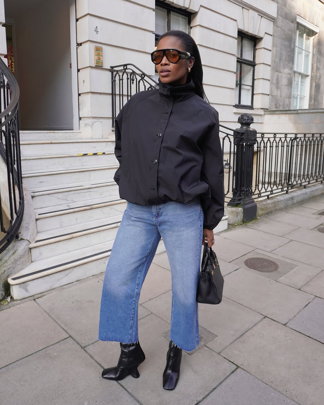 @nlmarilyn wearing black funnel neck jacket, wide-leg jeans, and black heeled boots