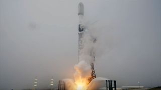a white and black rocket lifts off into the fog surrounding its launch pad