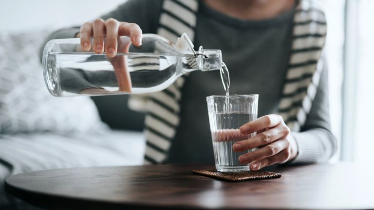 woman pouring herself a glass of water from a jug