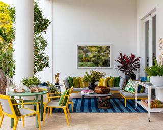 outdoor seating area with blue striped rug, yellow dining chairs, round green table and large gray sectional with yellow and green cushions