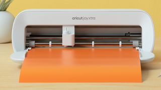 How to use a Cricut; a small craft machine on a table with orange paper
